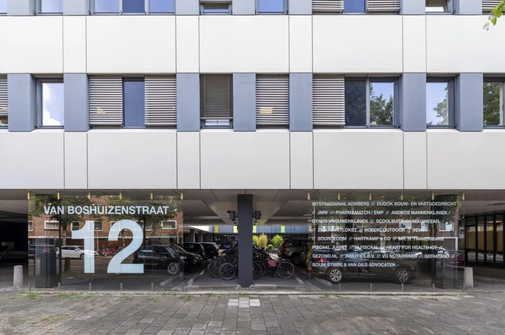 Entree van een kantoorgebouw aan de Van Boshuizenstraat 12 met namen van bedrijven op de glazen gevel.